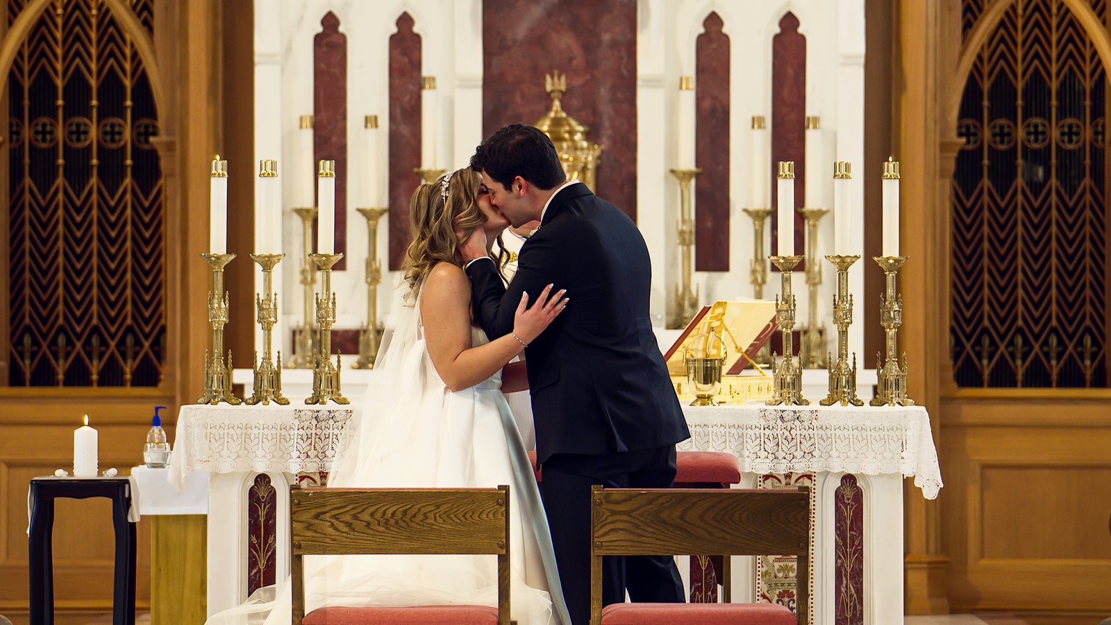 Casey and Matthew kissing during their wedding ceremony, surrounded by candles and gold church details